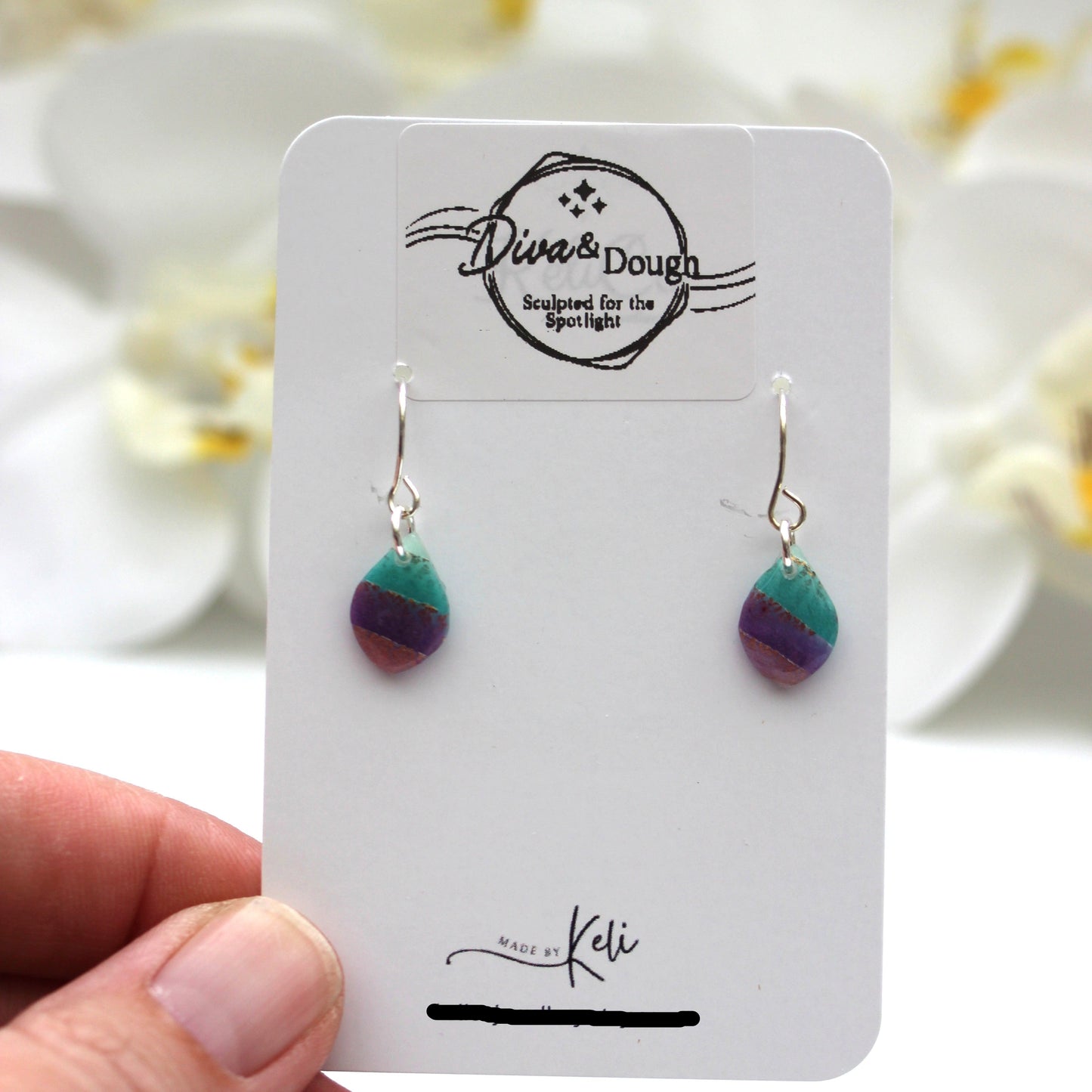 Colorful earrings on a branded card held by a hand with a soft focus background