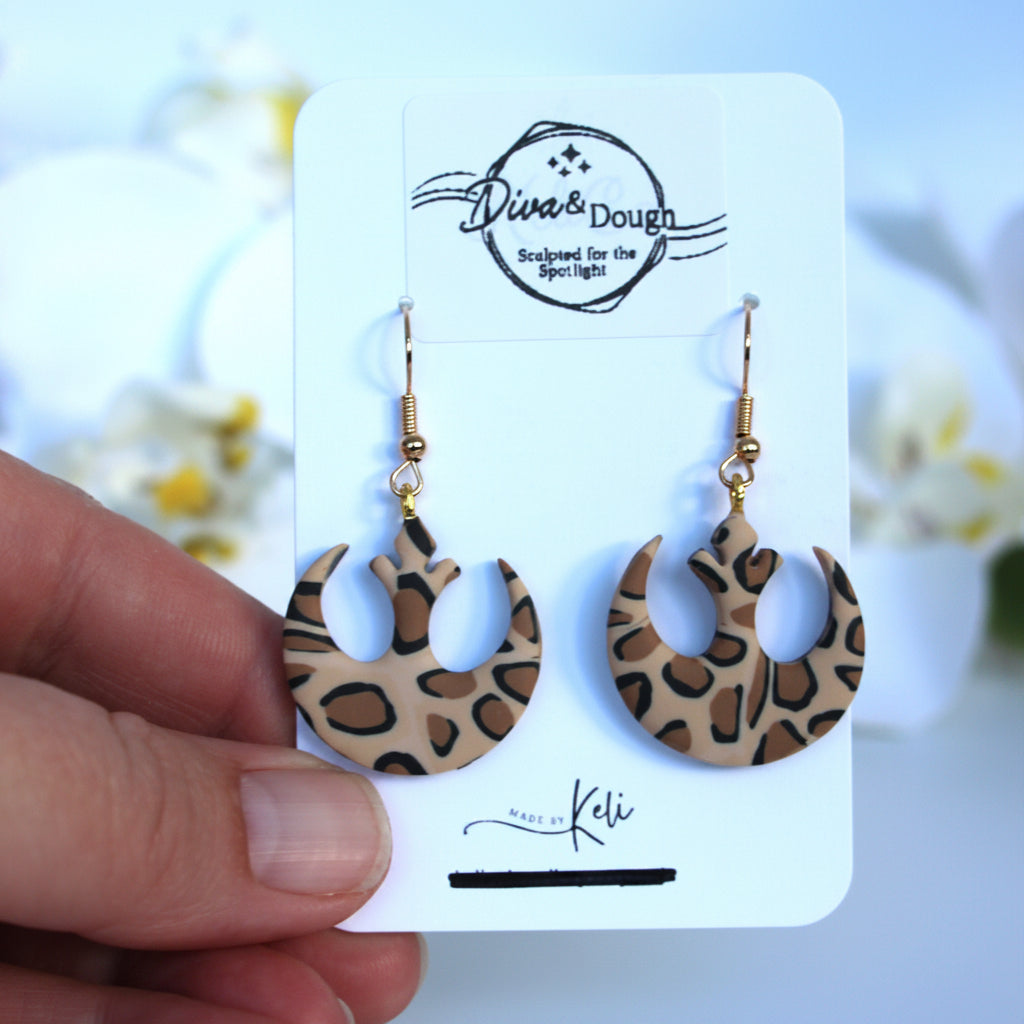 Leopard print earrings on a branded card held by a hand with a blurred floral background