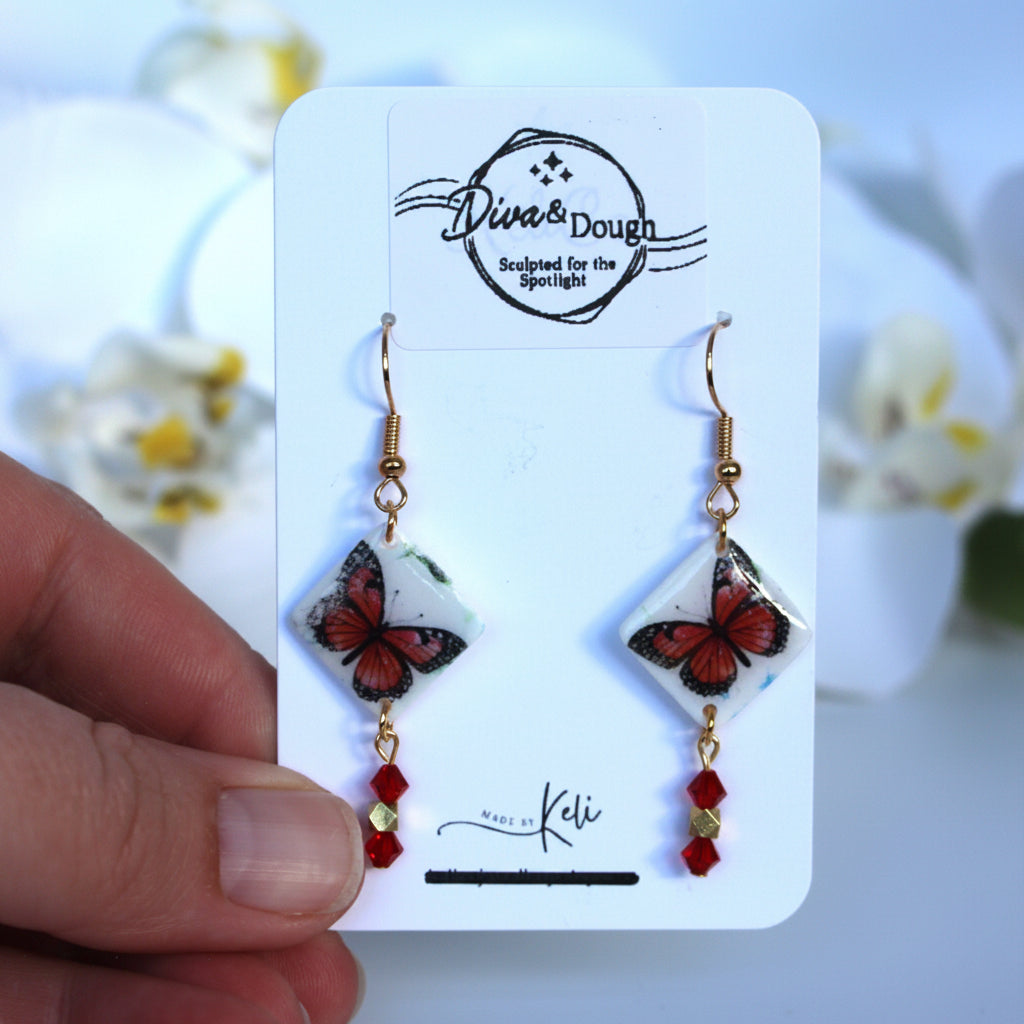 Butterfly earrings on a branded card held by a hand with a blurred floral background
