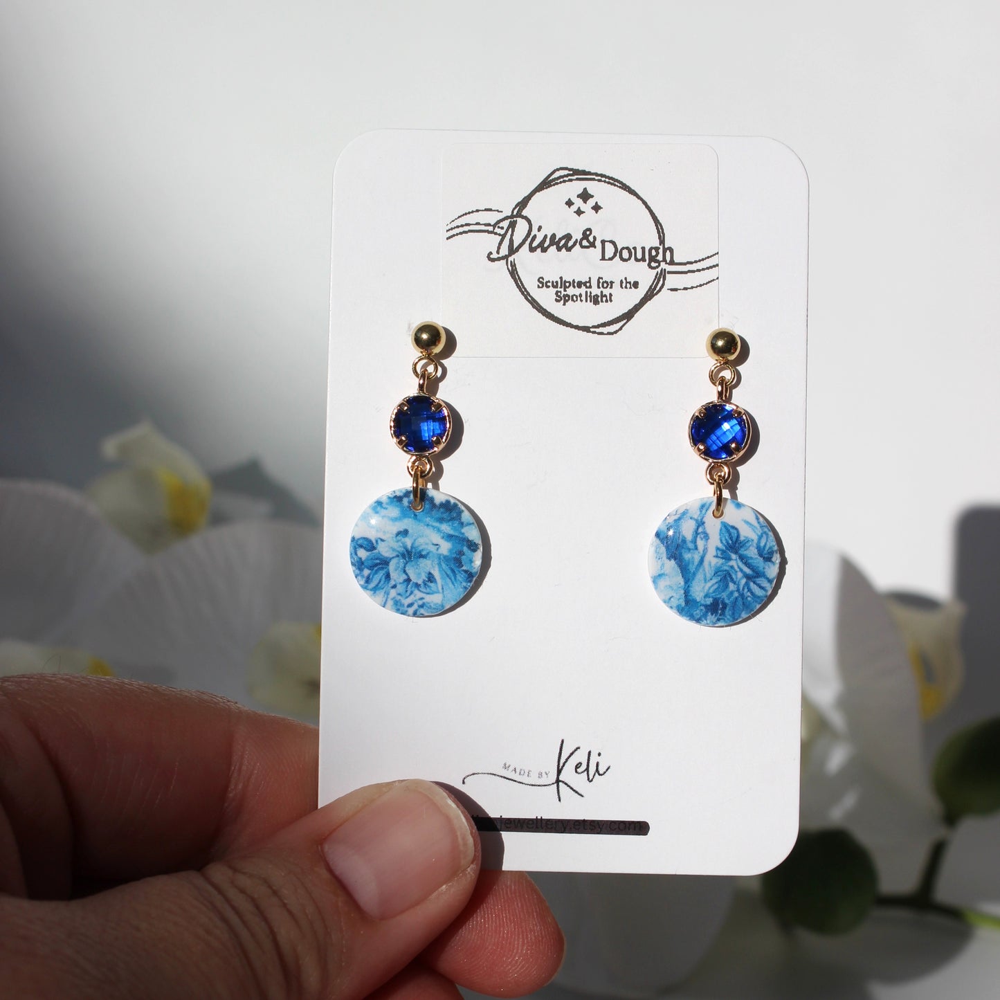 Blue and white earrings on a white card held by a hand with a blurred background