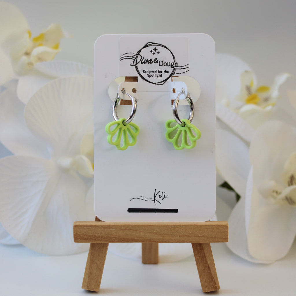 Green floral shaped earrings on a silver hoop on a display card with white orchids in the background