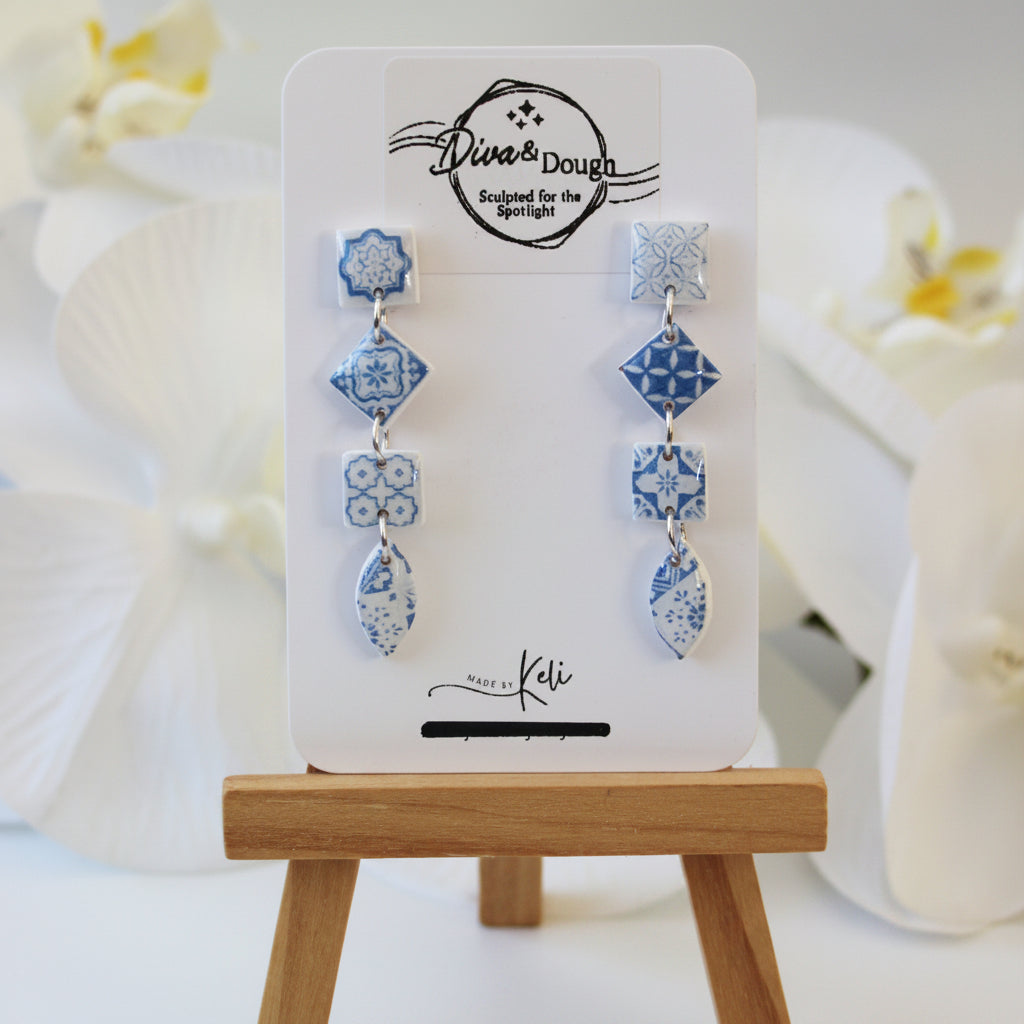 Set of blue floral earrings on a display card with a wooden stand.