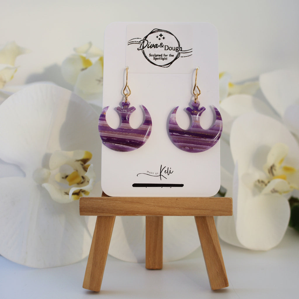 Purple earrings on a display card with a wooden stand against a white background