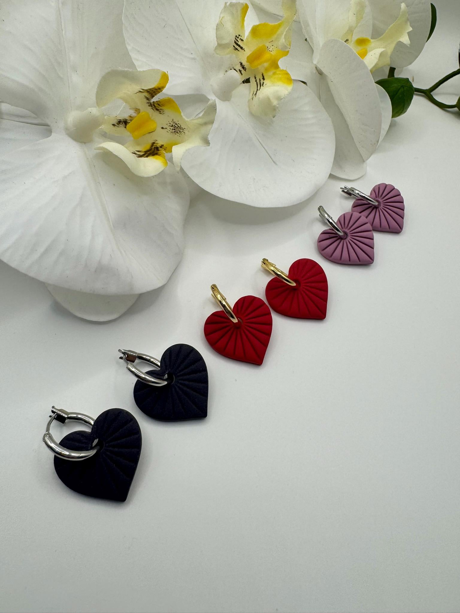 Heart-shaped earrings in black, red, and purple on a white surface with white flowers.