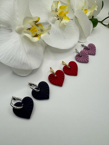 Heart-shaped earrings in black, red, and purple on a white surface with white flowers.