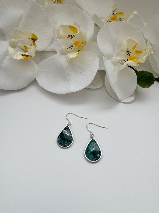 Teardrop-shaped earrings with silver hooks on a white surface with white flowers.