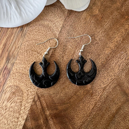 Black earrings on a wooden surface with white flowers in the background