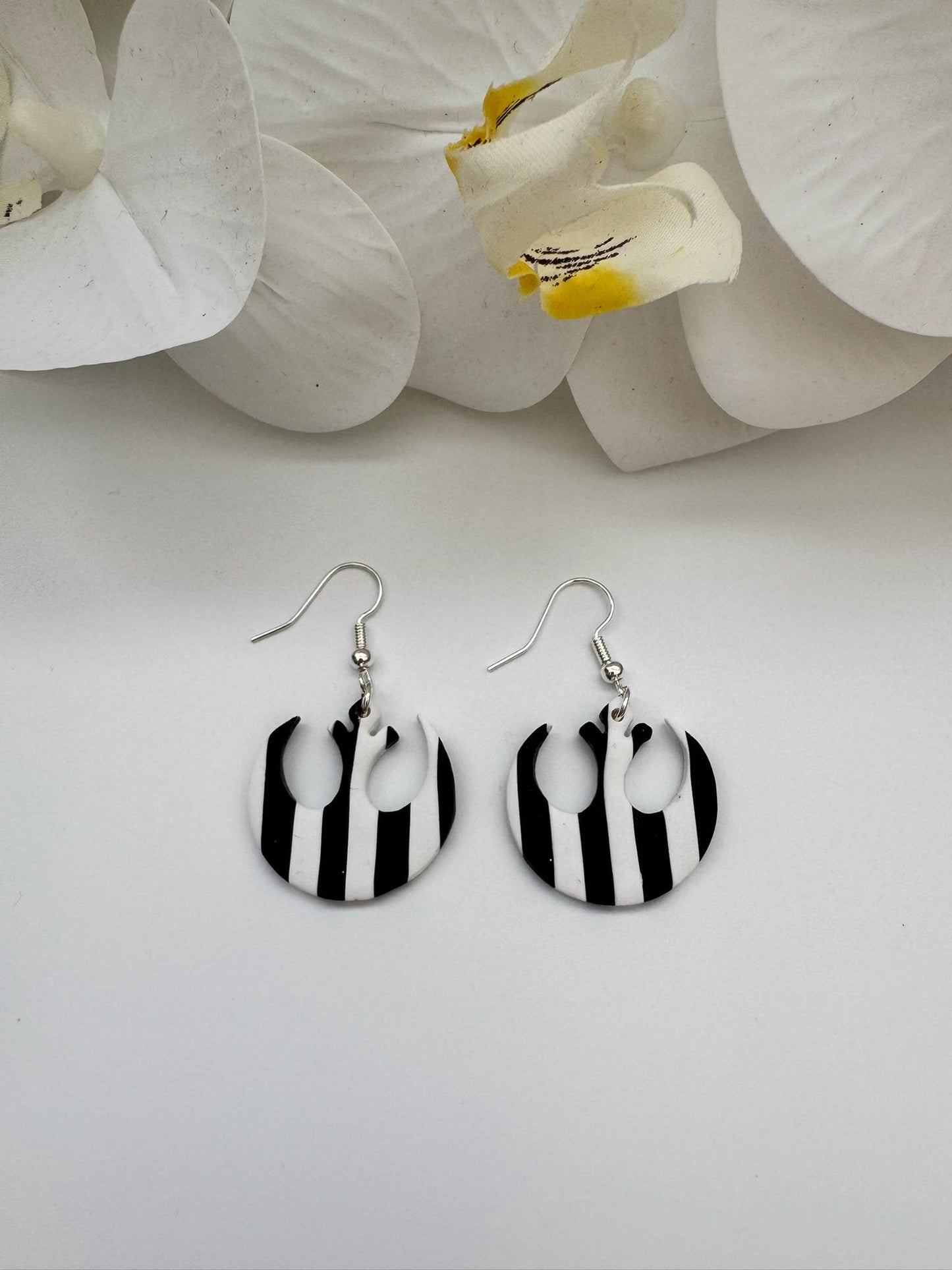 Black and white striped earrings on a light gray background with white orchids.