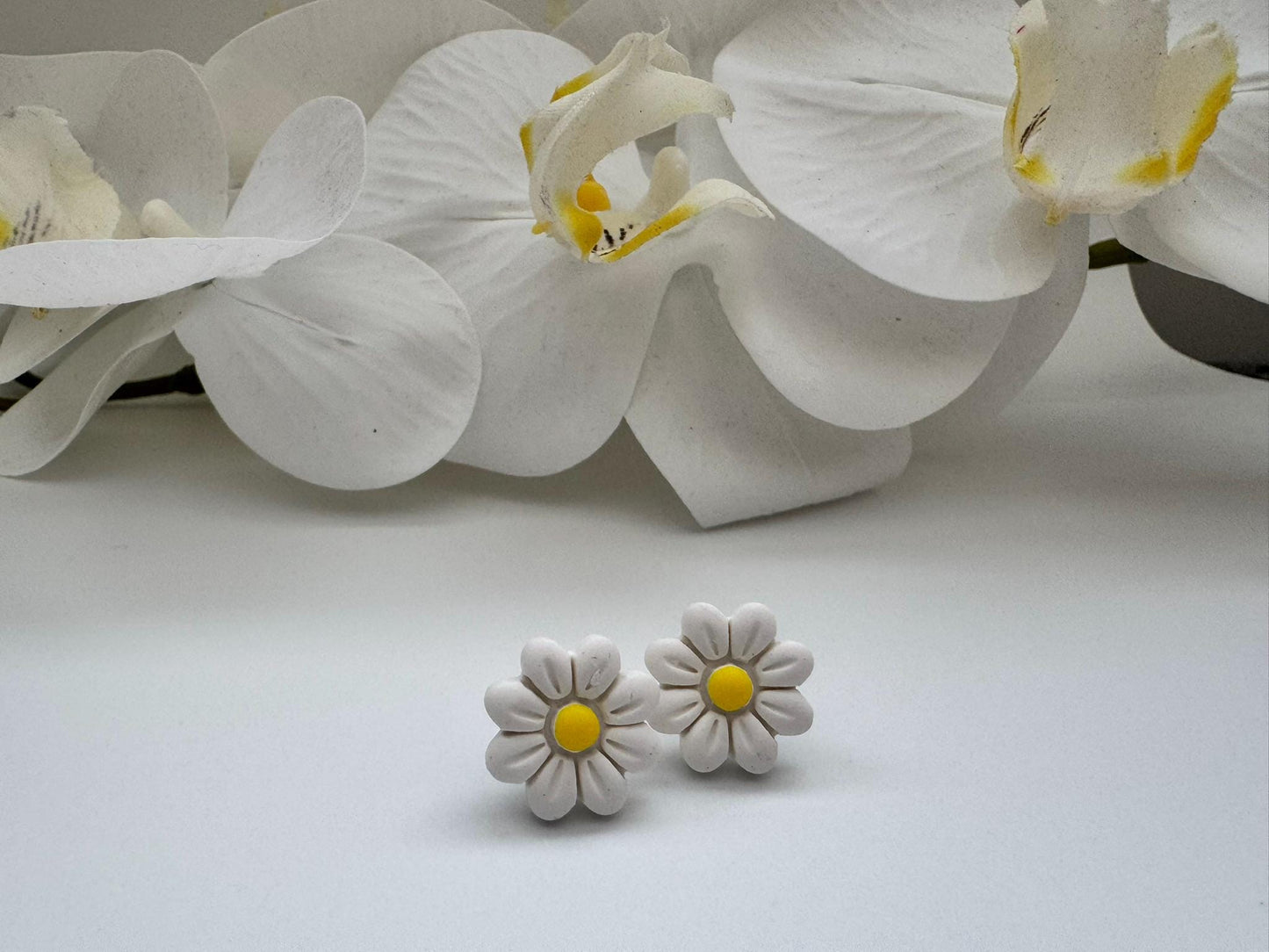 White daisy earrings with yellow centers on a white background