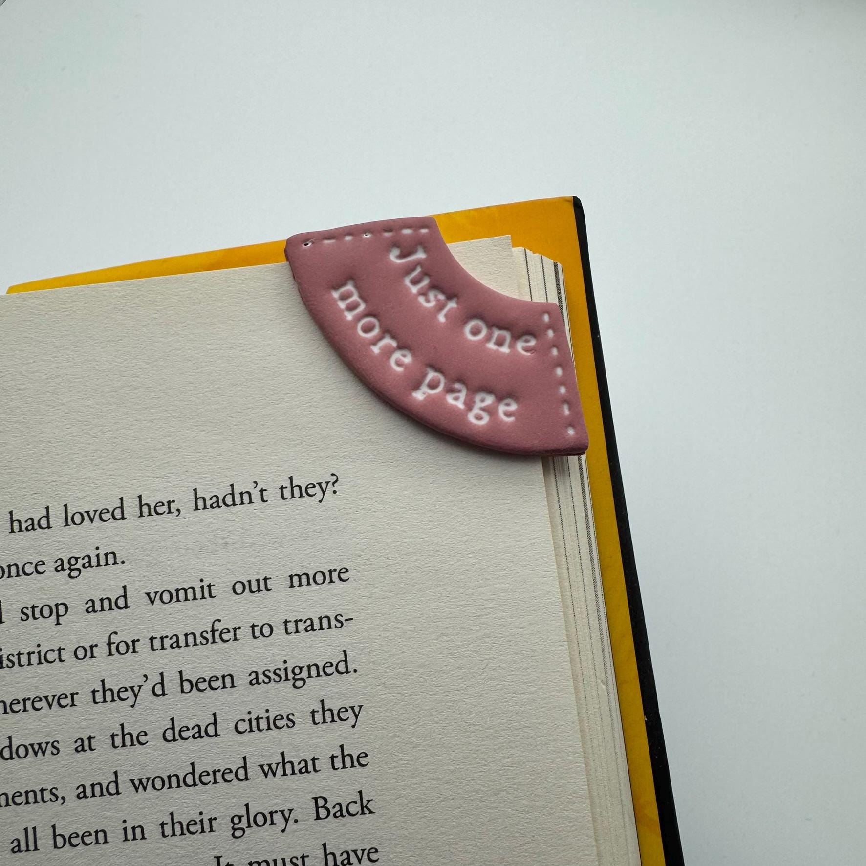 Book with a pink leather bookmark labeled 'Just one more page' on a white background