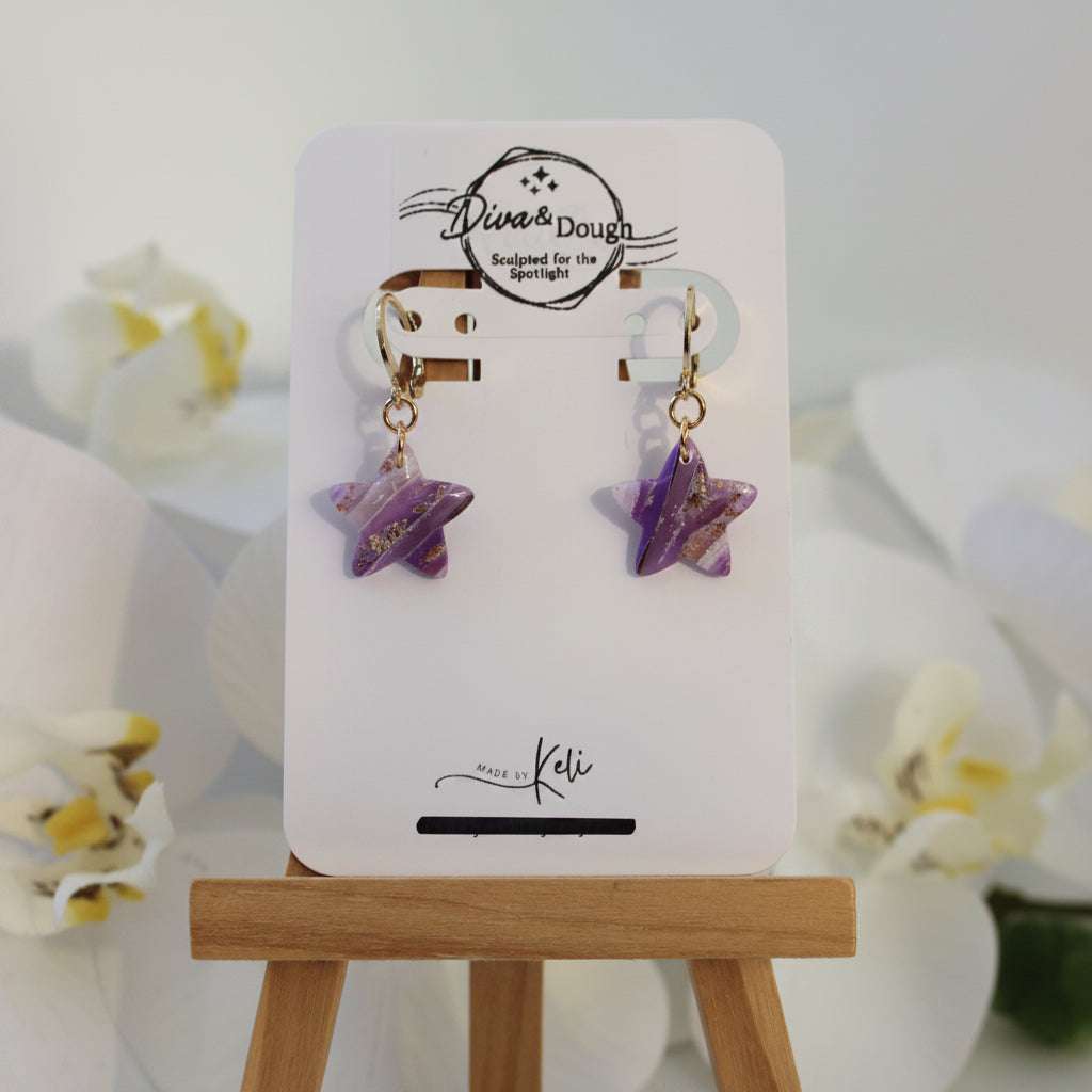 Star-shaped earrings on a display card with a wooden stand, against a light background.