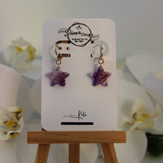 Star-shaped earrings on a display card with a wooden stand, against a light background.