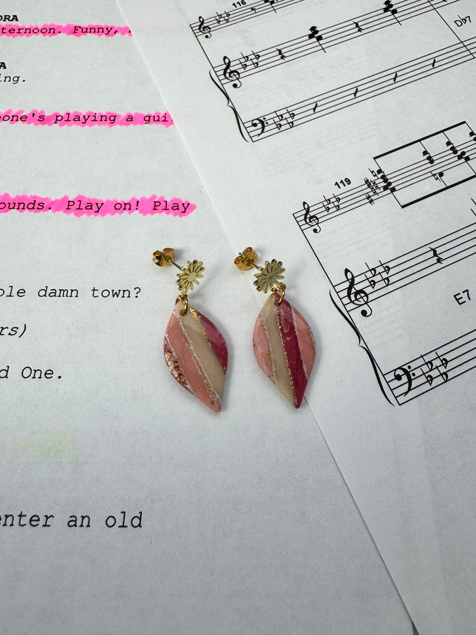 Pair of pink and gold earrings on a sheet of music.