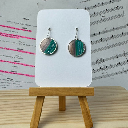 Striped earrings in a silver coloured circle bezel, on a display card with a wooden stand, set against a background of sheet music.