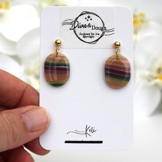 Pair of earrings on a 'Dive & Dough' branded card held by a hand with a blurred floral background.
