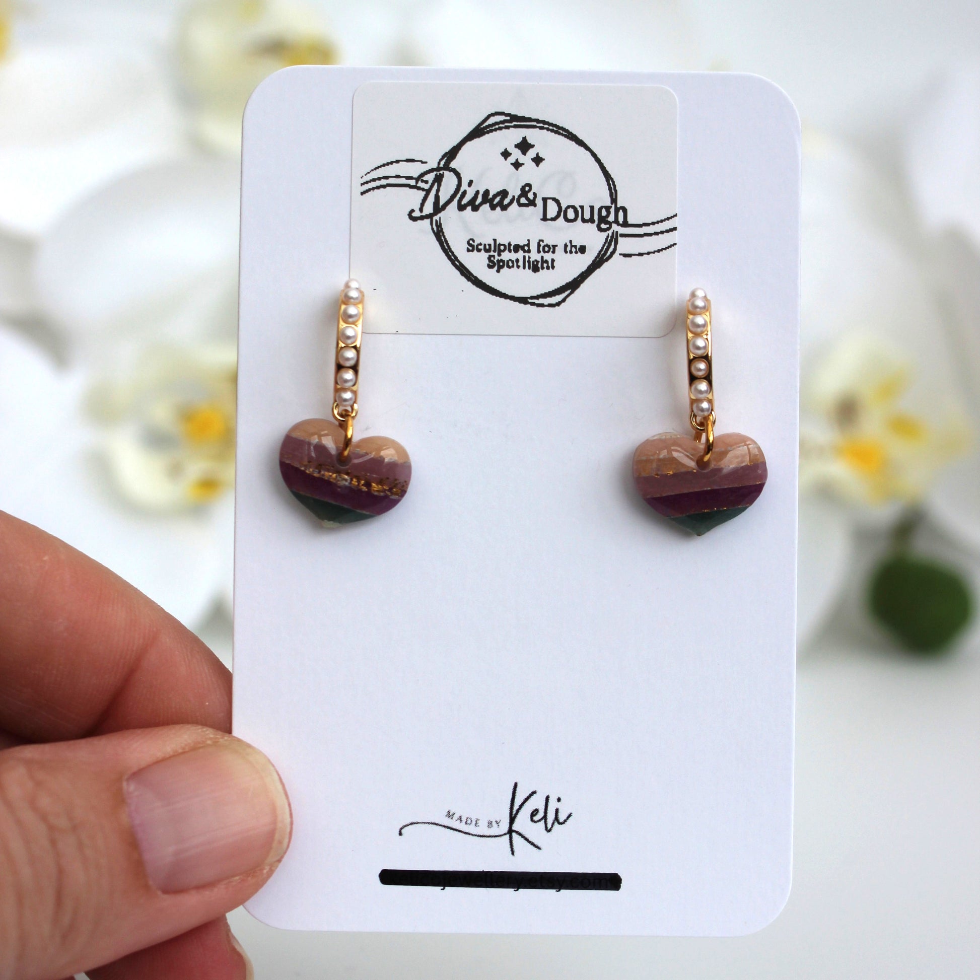 Heart-shaped earrings on a branded card held by a hand with a blurred floral background
