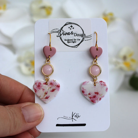 Heart-shaped earrings on a 'Diva & Dough' branded card with a blurred floral background.