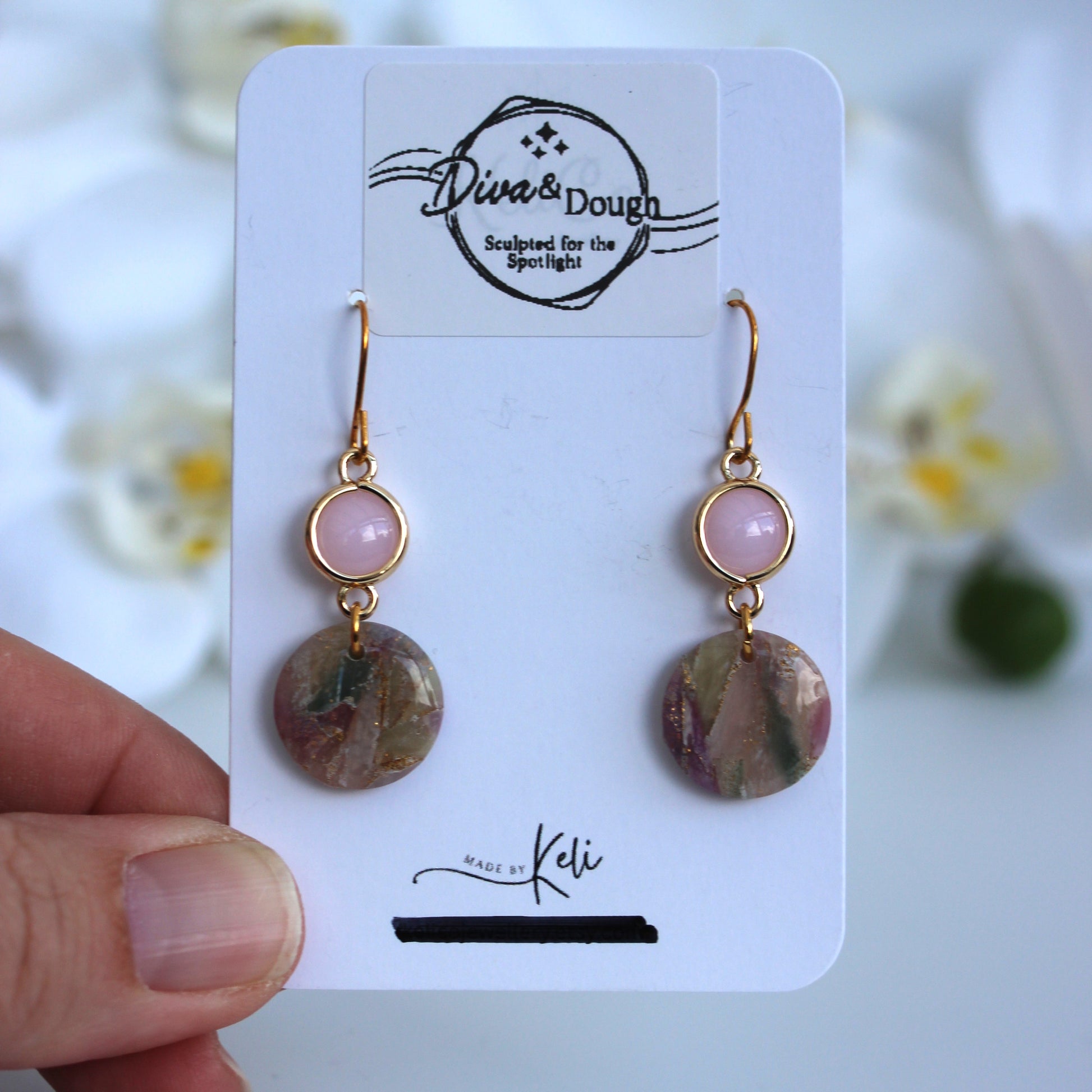 Earrings on a Diva & Dough branded card held by a hand with a blurred floral background