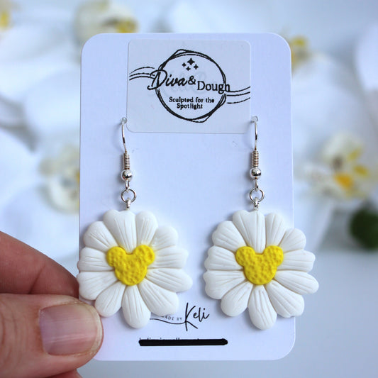White flower-shaped earrings with a yellow mouse ears shaped center on a branded card held by a hand.