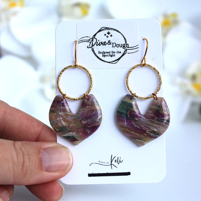 Multicolored heart-shaped earrings on a branded card held by a hand.