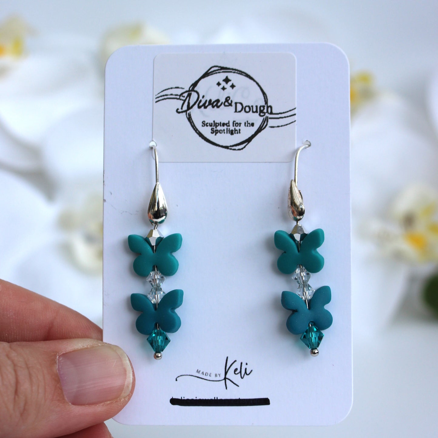 Turquoise butterfly earrings on a branded card held by a hand with a blurred floral background