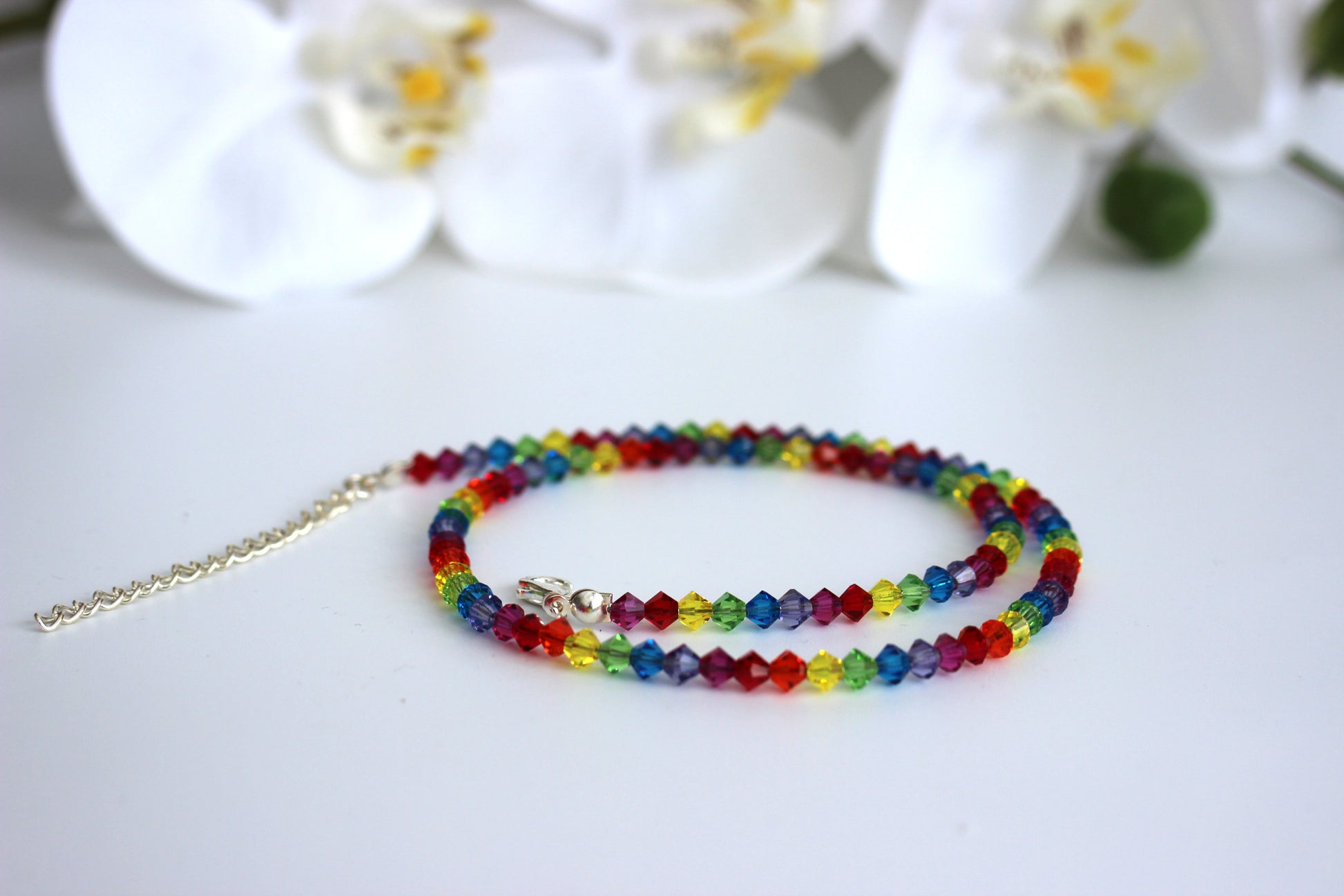 Colorful beaded necklace on a white surface with blurred flowers in the background