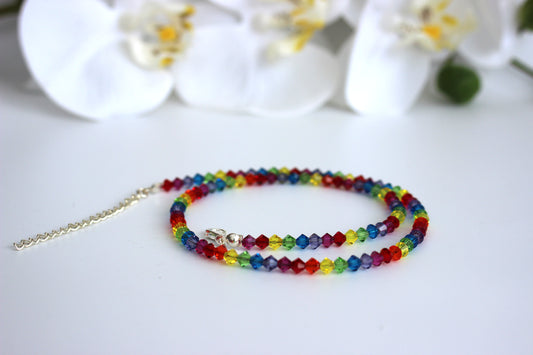 Colorful beaded necklace on a white surface with blurred flowers in the background