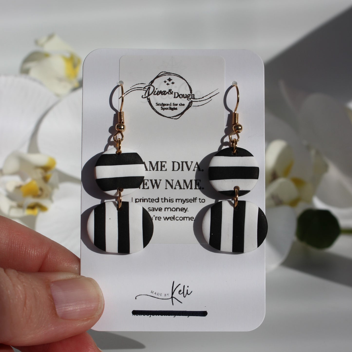 Black and white striped earrings on a branded card held by a hand with a blurred floral background.