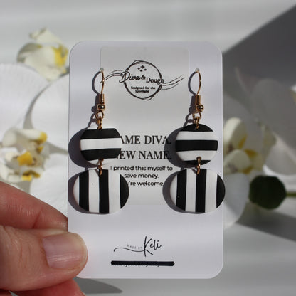 Black and white striped earrings on a branded card held by a hand with a blurred floral background.