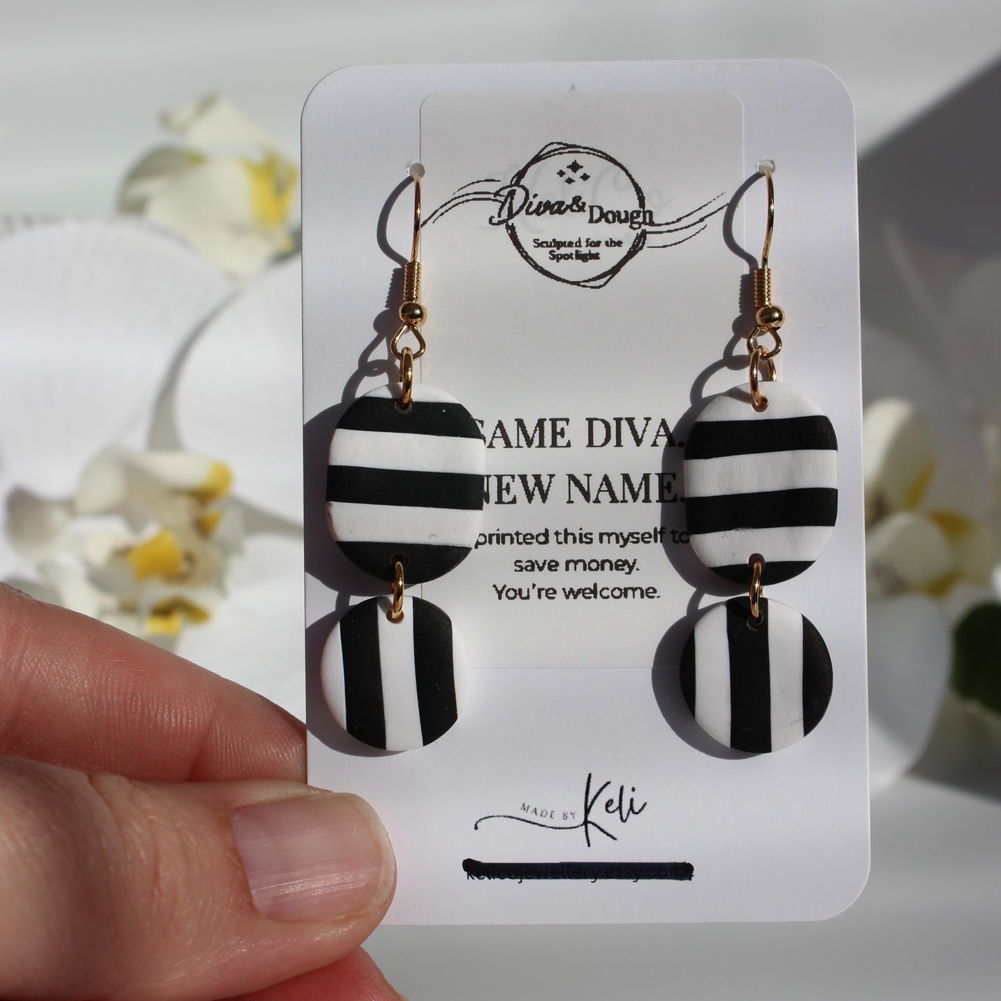 Black and white striped earrings on a branded card held by a hand with a blurred floral background