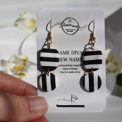 Black and white striped earrings on a branded card held by a hand with a blurred floral background