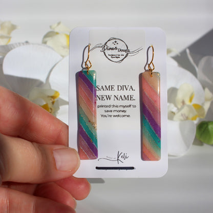 Colorful striped earrings on a branded card held by a hand with a floral background