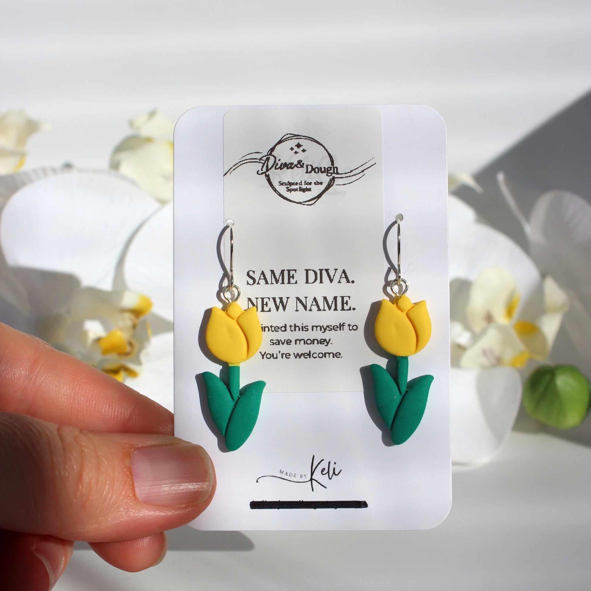 Yellow tulip-shaped earrings on a branded card held by a hand with flowers in the background