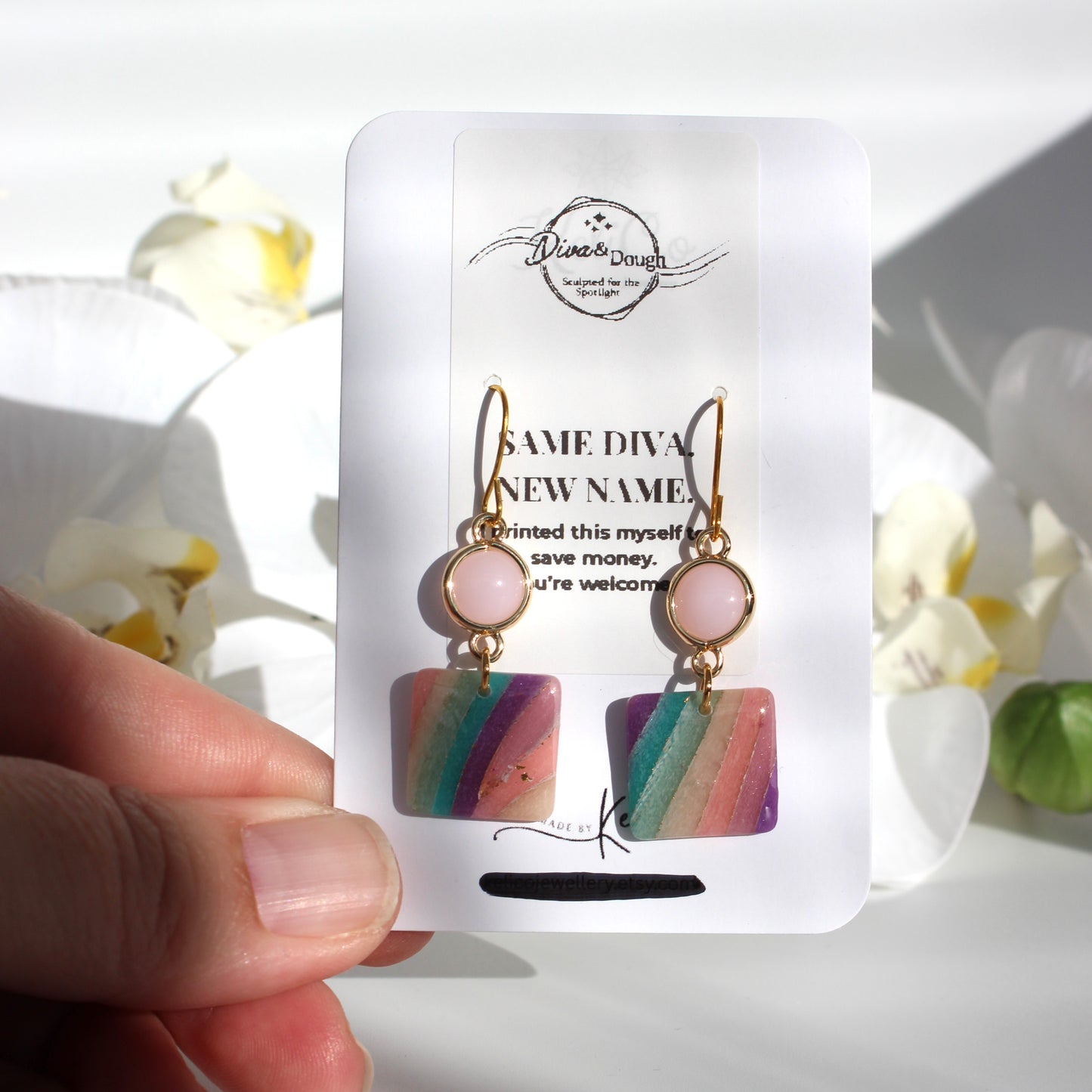 Colorful earrings on a white card held by a hand with a floral background