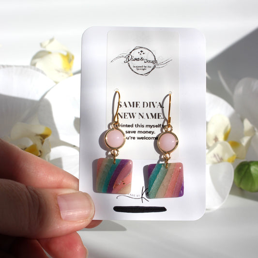 Colorful earrings on a white card held by a hand with a floral background