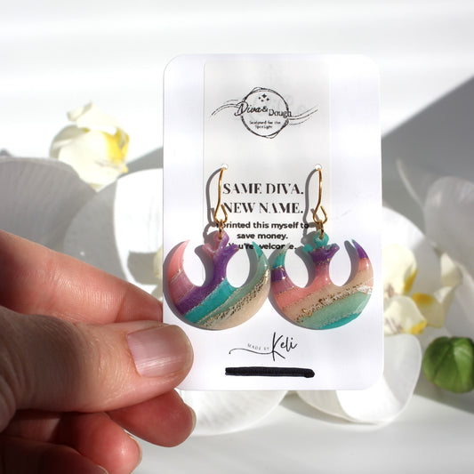 Colorful earrings on a branded card held by a hand with a blurred floral background