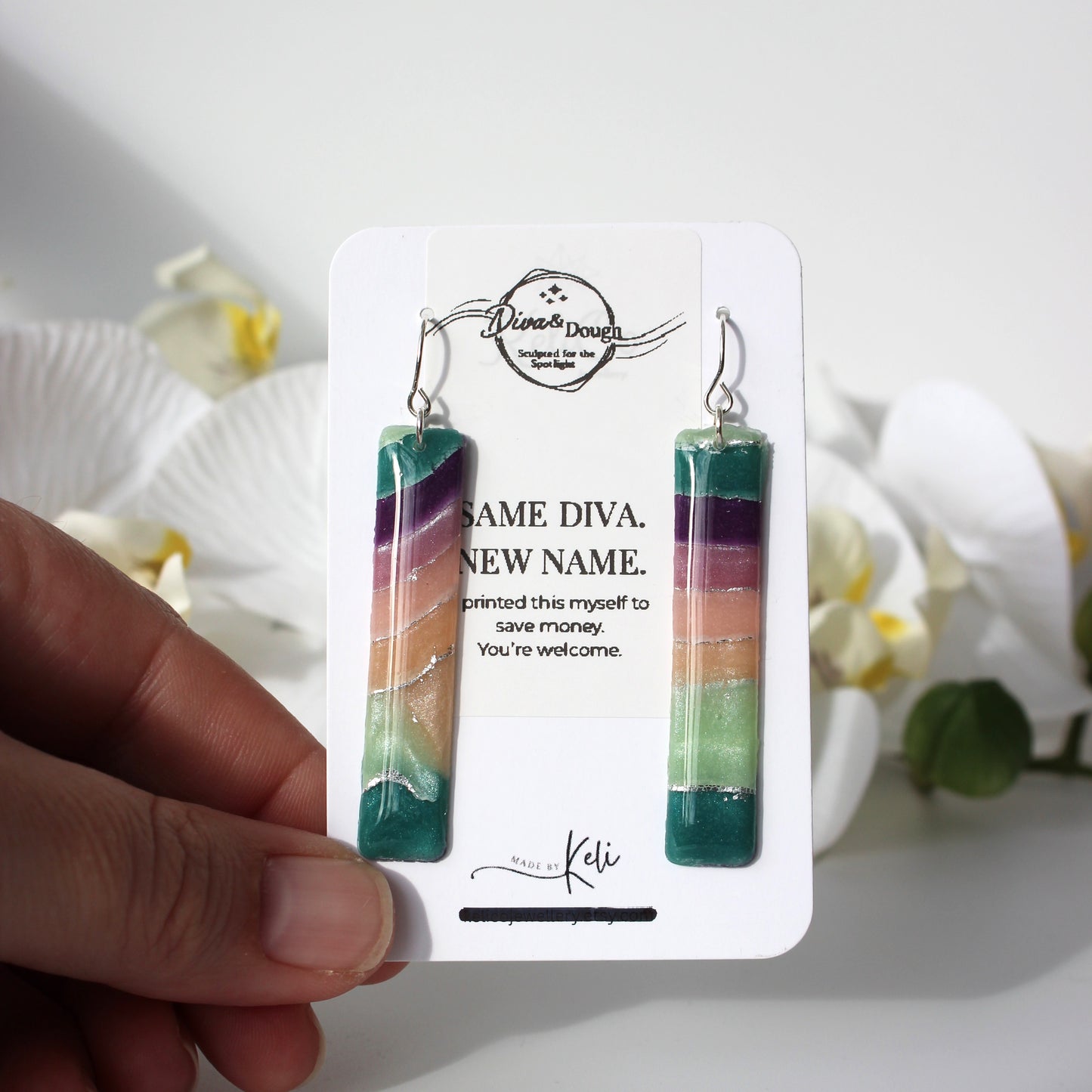 Colorful earrings on a branded card held by a hand with a floral background