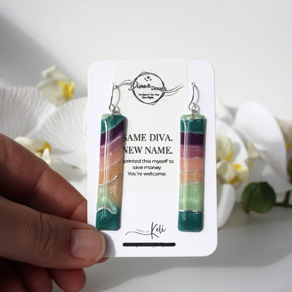 Colorful earrings on a branded card held by a hand with a floral background