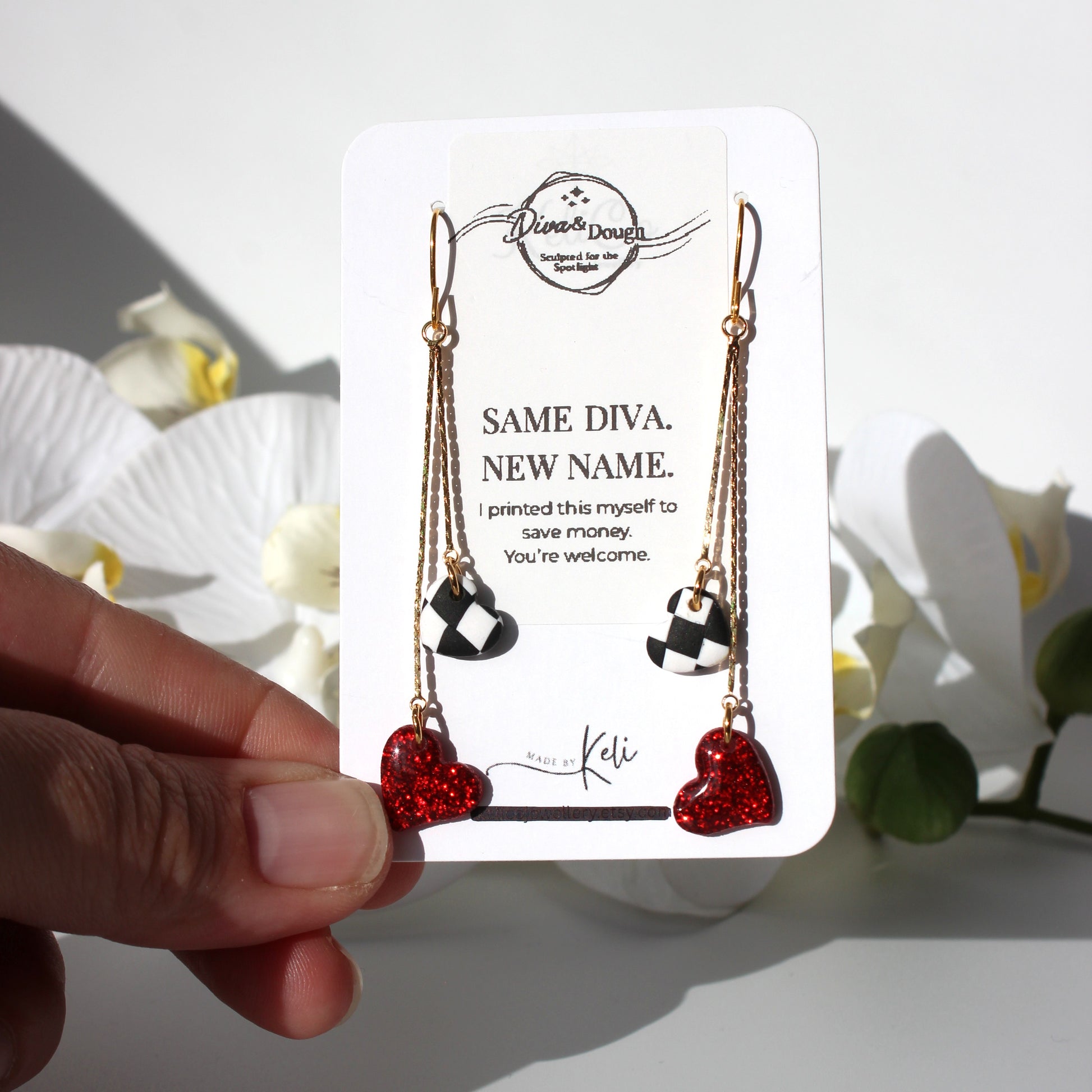 Heart-shaped earrings on a branded card held by a hand with flowers in the background