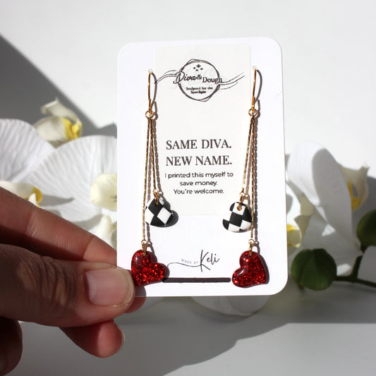 Heart-shaped earrings on a branded card held by a hand with flowers in the background