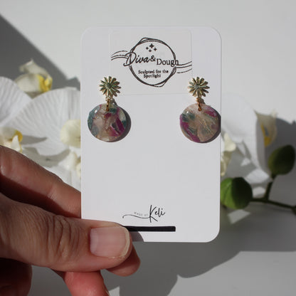 Floral earrings on a 'Diva & Dough' branded card held by a hand with a white background.