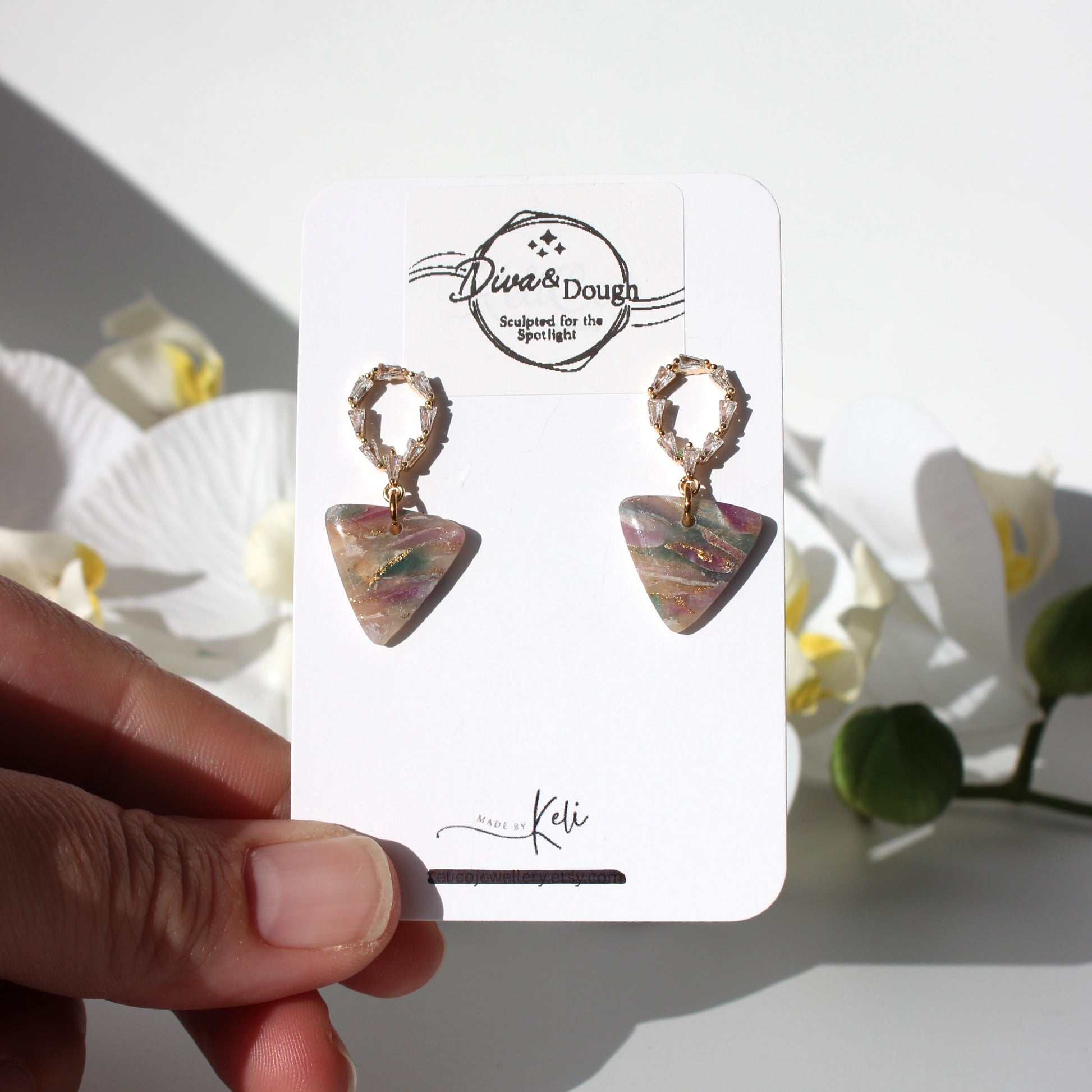 Pair of earrings on a branded card held by a hand with a floral background