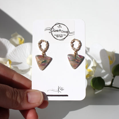 Pair of earrings on a branded card held by a hand with a floral background