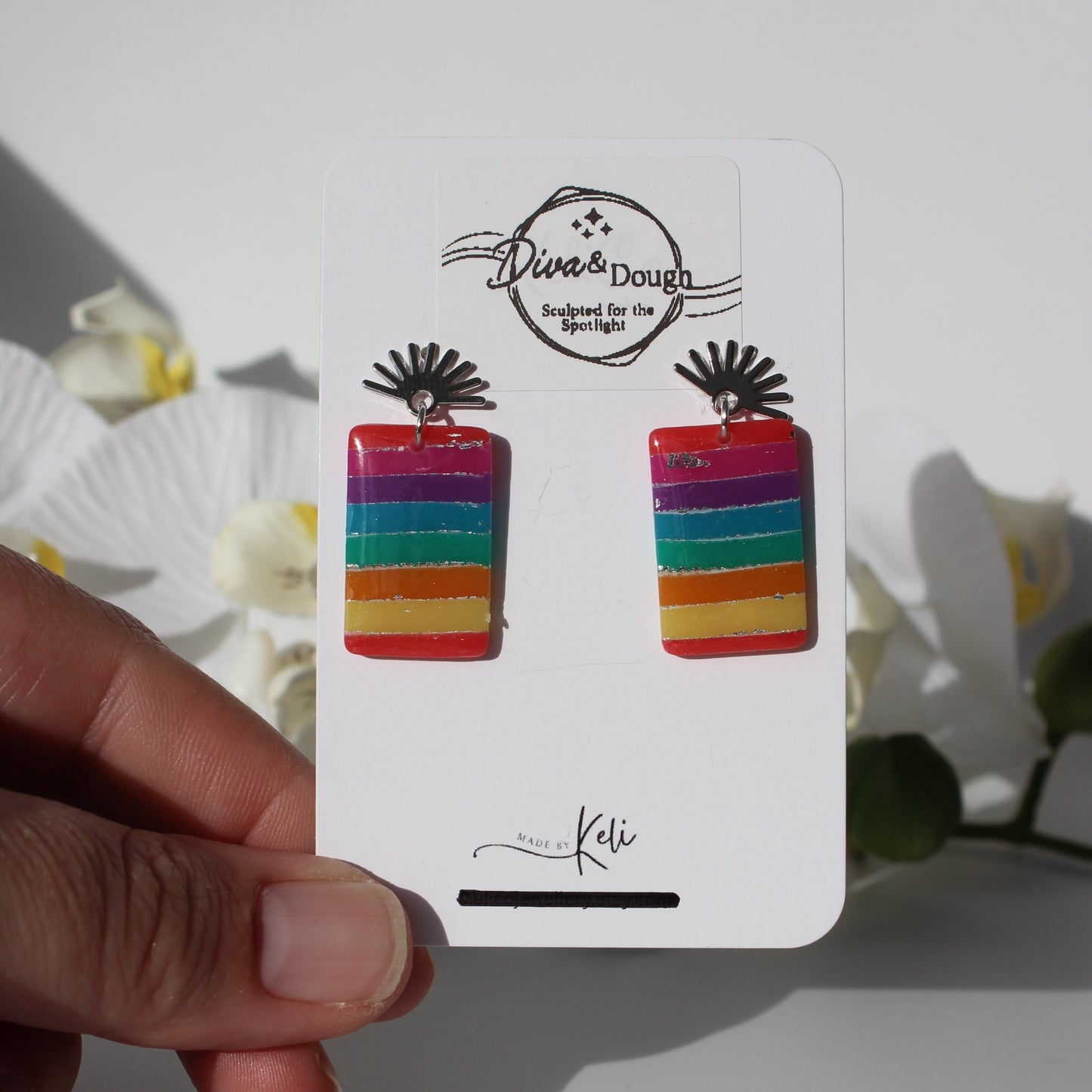 Colorful striped earrings on a branded card held by a hand with a soft background
