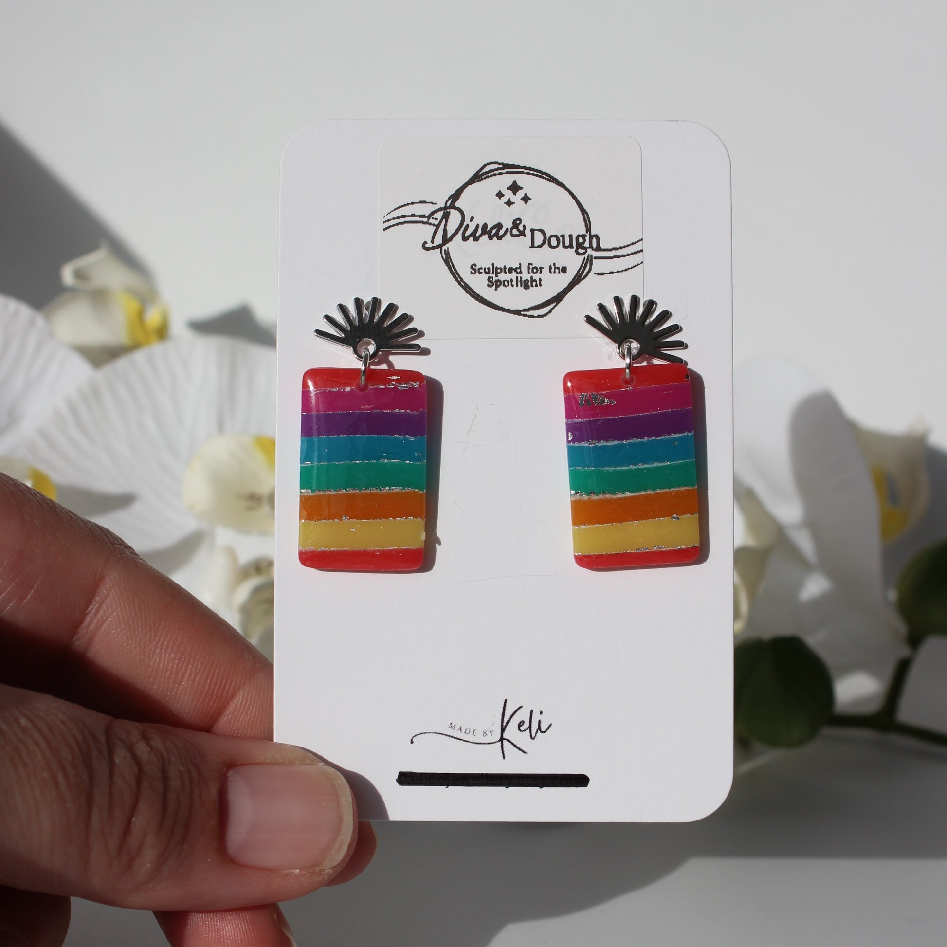 Colorful striped earrings on a branded card held by a hand with a soft background