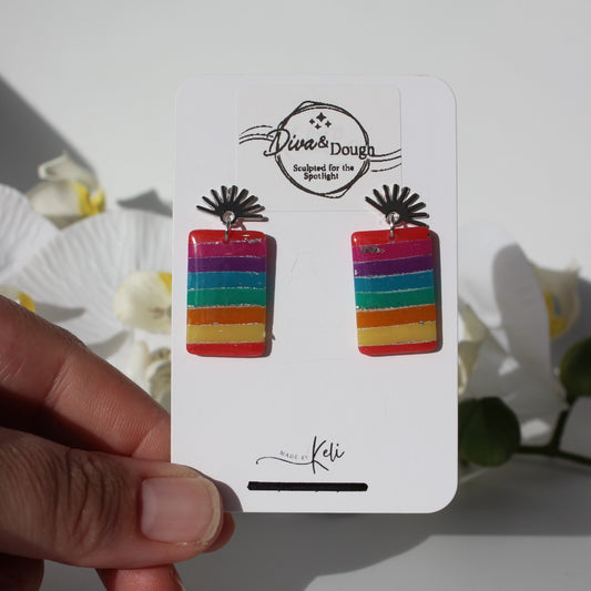 Colorful striped earrings on a branded card held by a hand with a soft background
