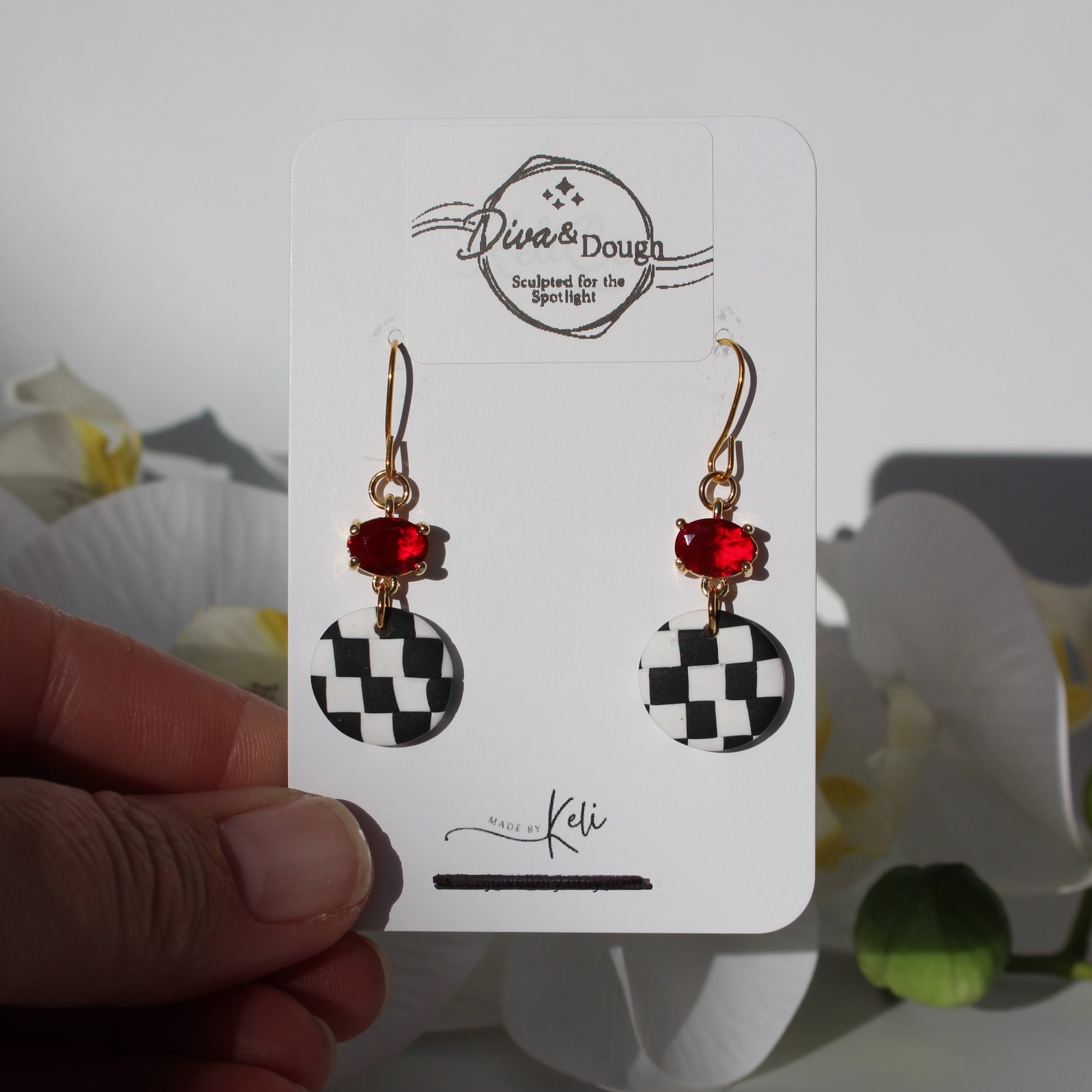 Pair of earrings on a 'Diva & Dough' branded card held by a hand with a blurred background.