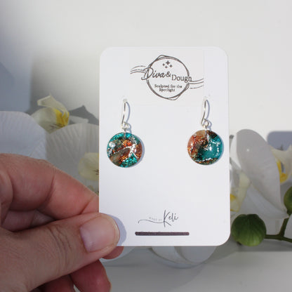 Colorful earrings on a branded card held by a hand with a white background