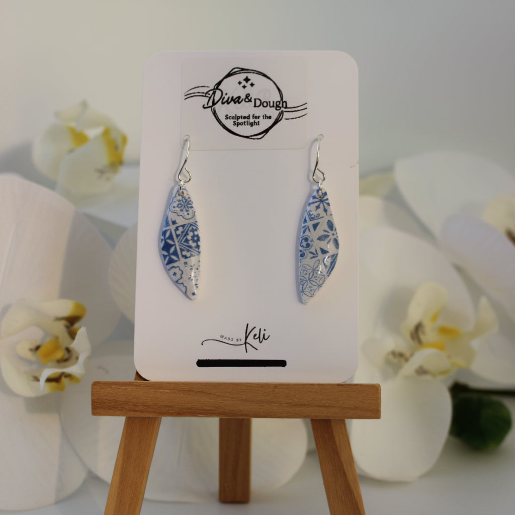 Pair of earrings on a card with a wooden stand against a white background