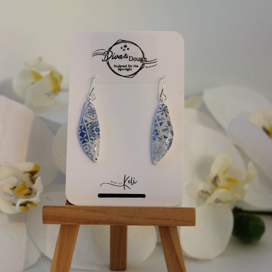 Pair of earrings on a card with a wooden stand against a white background